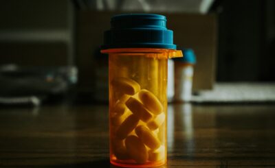 A prescription bottle containing yellow pills on a wooden surface, with blurred background elements, indicating medicati