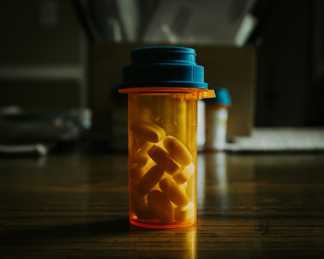 A prescription bottle containing yellow pills on a wooden surface, with blurred background elements, indicating medicati